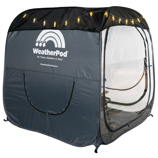 A WeatherPod pop-up tent pod in dark gray with a black detachable roof, featuring a clear PVC, string lights along the top, and the WeatherPod logo printed on the back.