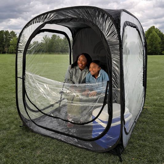 A mother and daughter inside a MegaPod Plus pop-up tent on grass with trees in the background.