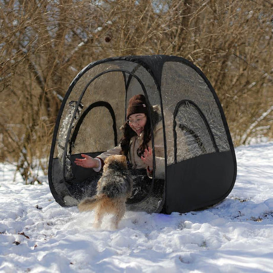 Black pop-up canopy tent with transparent plastic windows, shown with dimension lines indicating 42 inches height and 36 inches width and depth with a female and her dog in the snow.